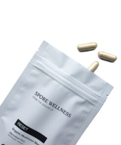 Spore Wellness brand Reset container standing next to several two piece vegetable capsules